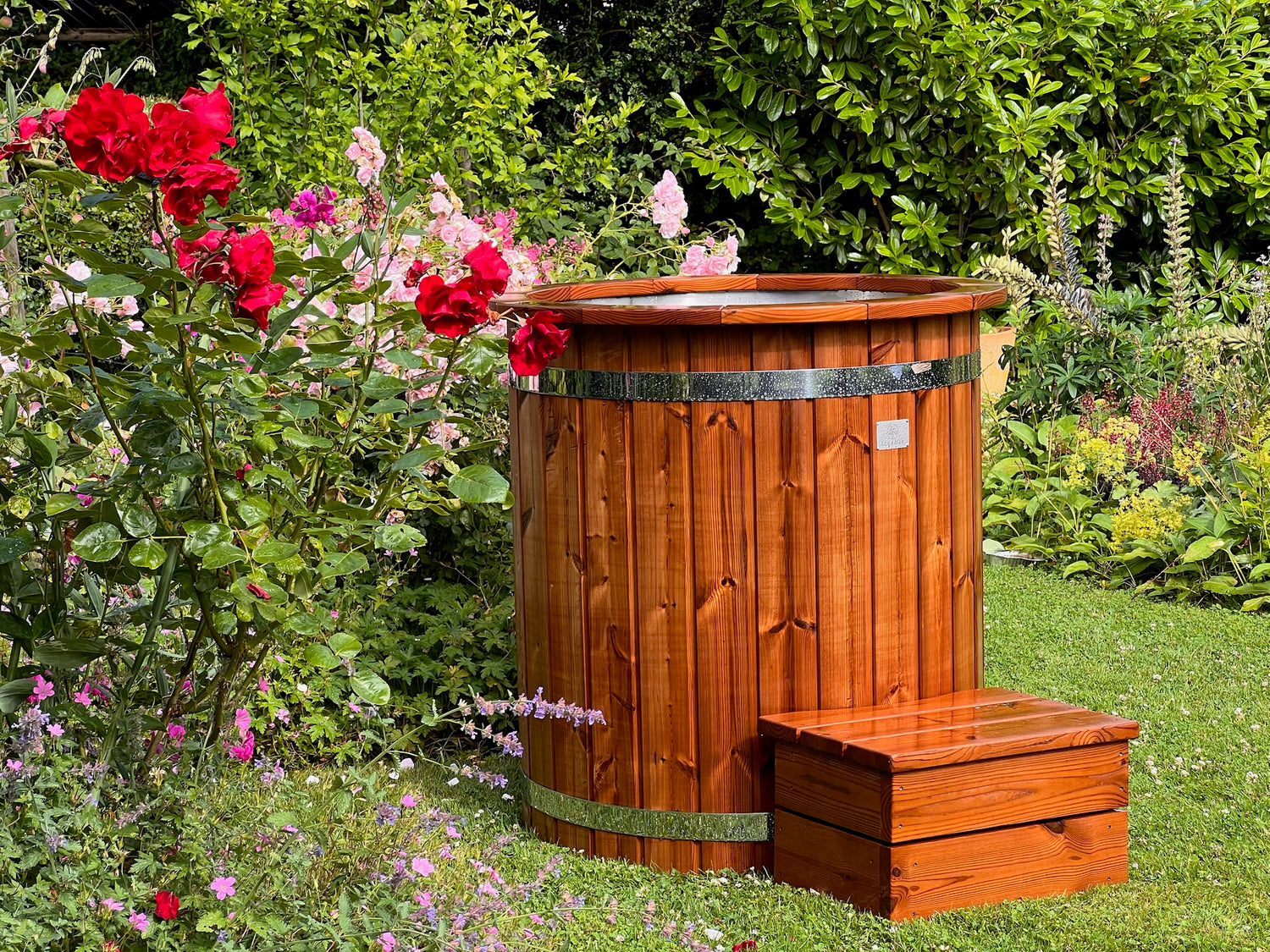 Træ isbad i frodig have med røde og lyserøde blomster