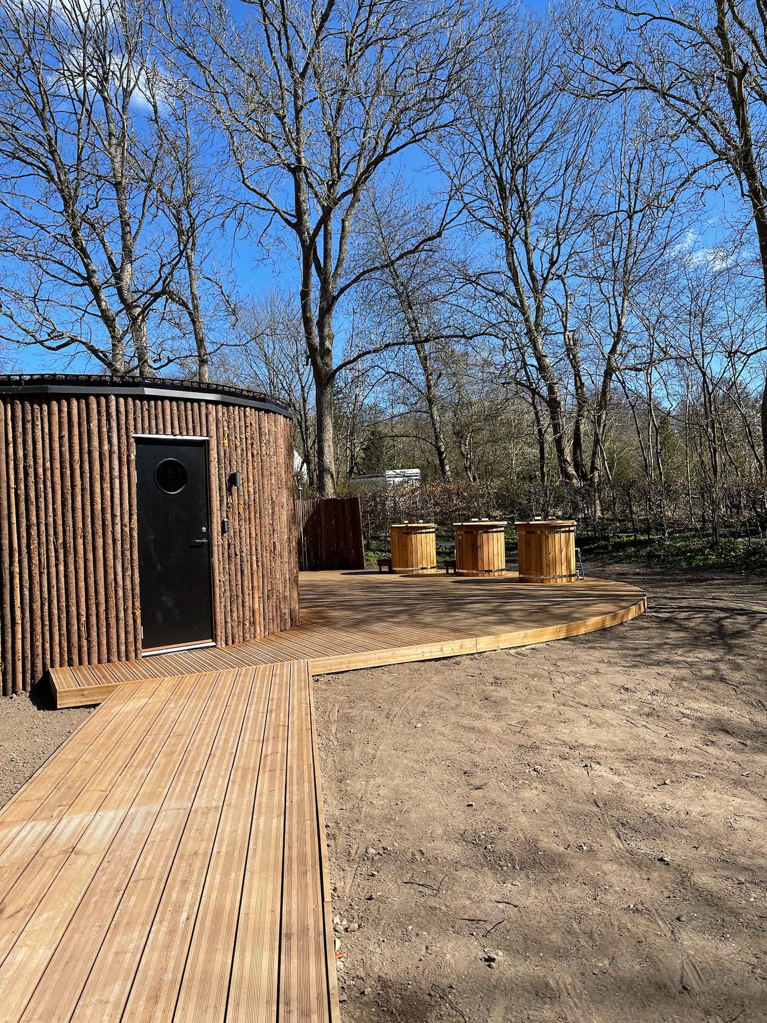 Isbad i træ med sort dør og træterrasse ude i naturen.