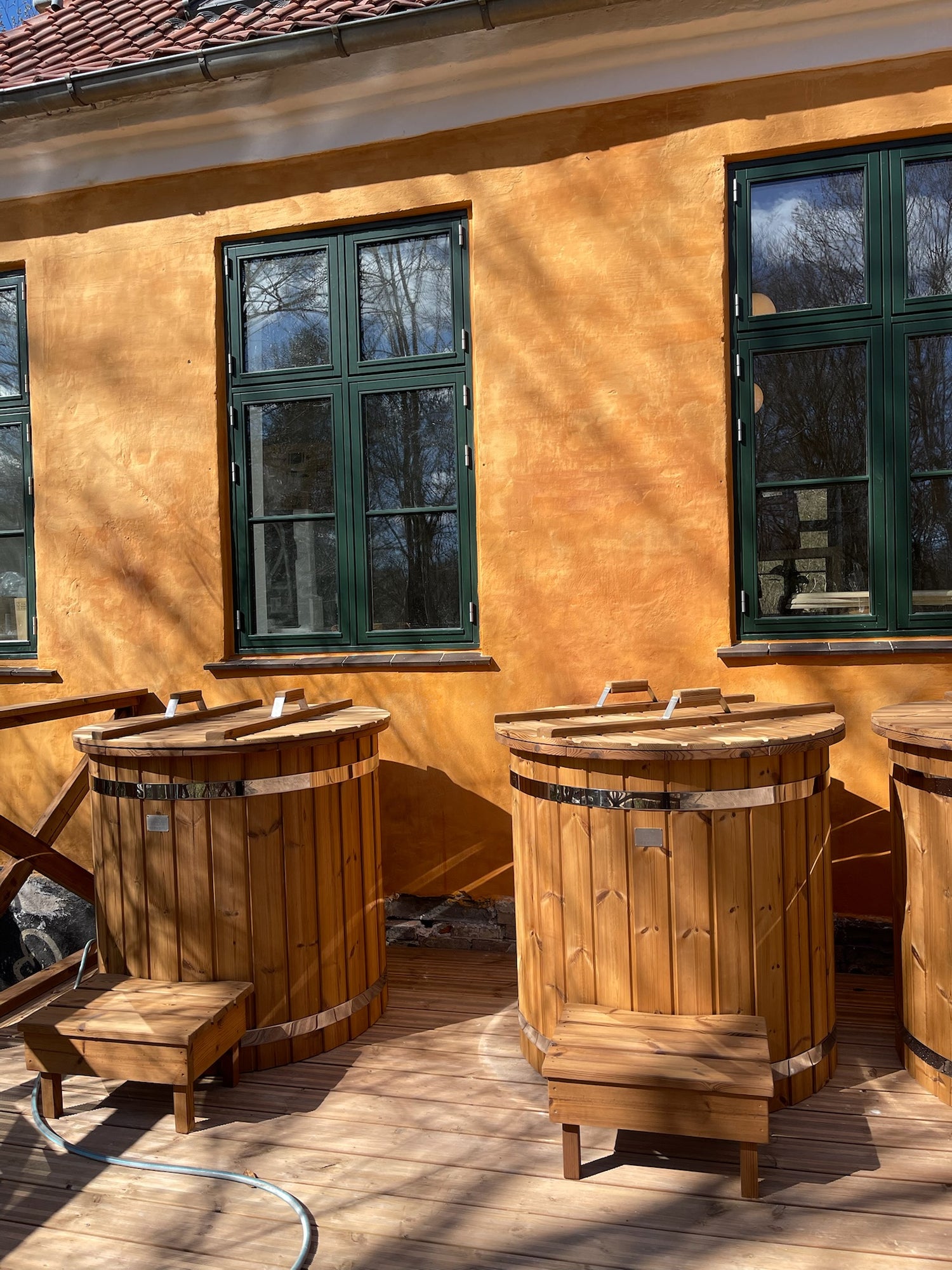 To icebade i træ med låg og trappetrin foran en gul bygning med grønne vinduer